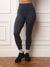 A person wearing dark charcoal gray high-waisted leggings, white socks, and black athletic shoes, standing against a white paneled wall on a wooden floor.