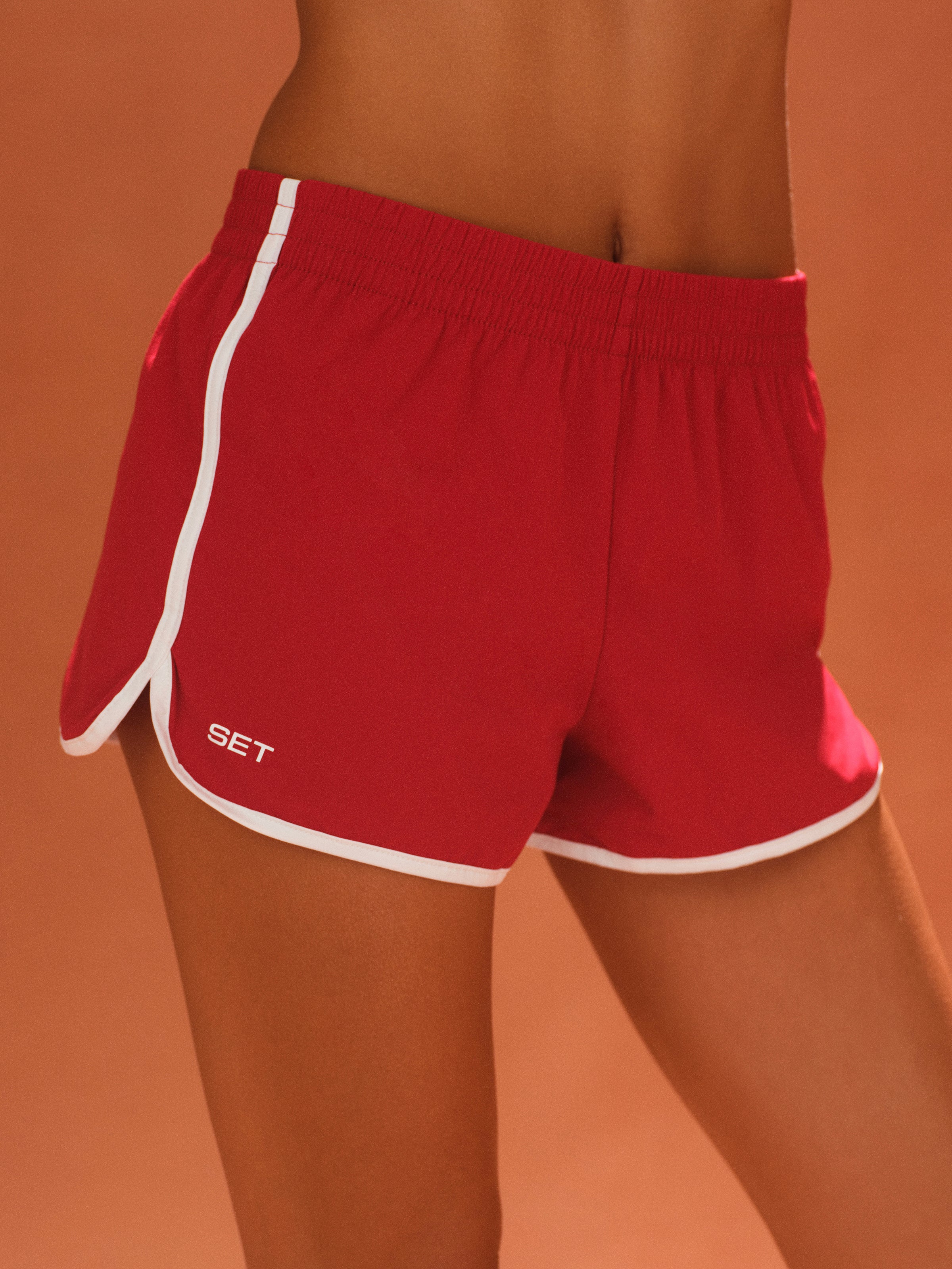 Red shorts with white trim on a person against an orange background 