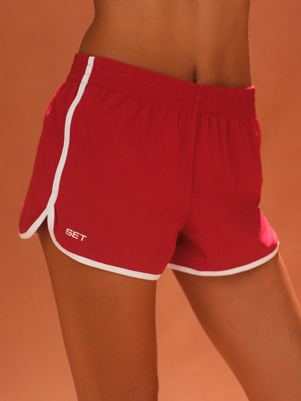 Red shorts with white trim on a person against an orange background 