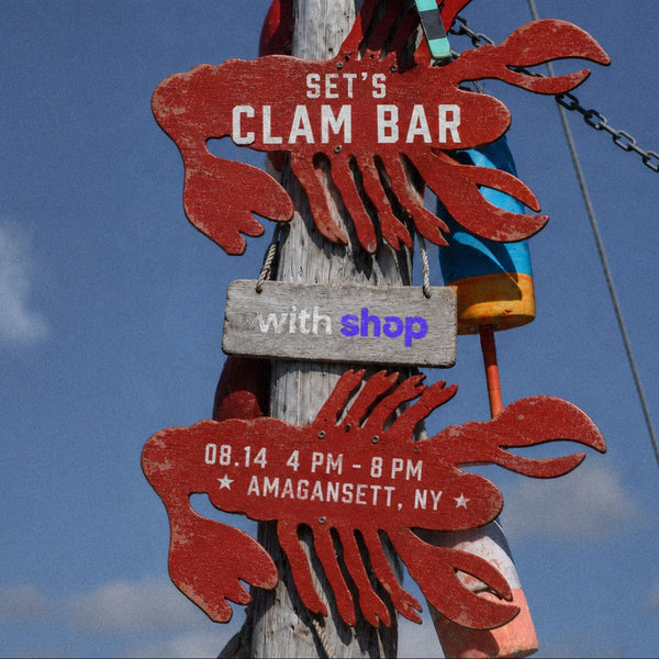 A weathered wooden post outdoors with two red lobster-shaped signs reading 'SET'S CLAM BAR' and 'with shop', plus a turquoise buoy and blue sky in the background.