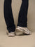 A close-up of a person's legs wearing dark navy pants and chunky white and gray sneakers with black laces, standing against a plain beige studio background.
