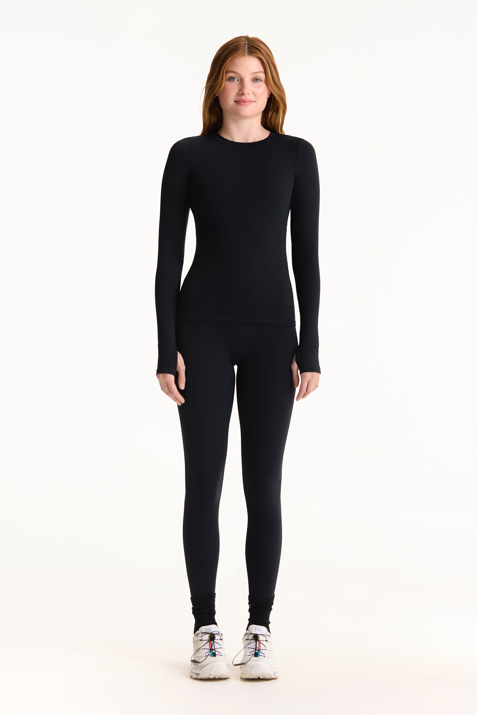 Person wearing a black long-sleeve top and black leggings on a white background
