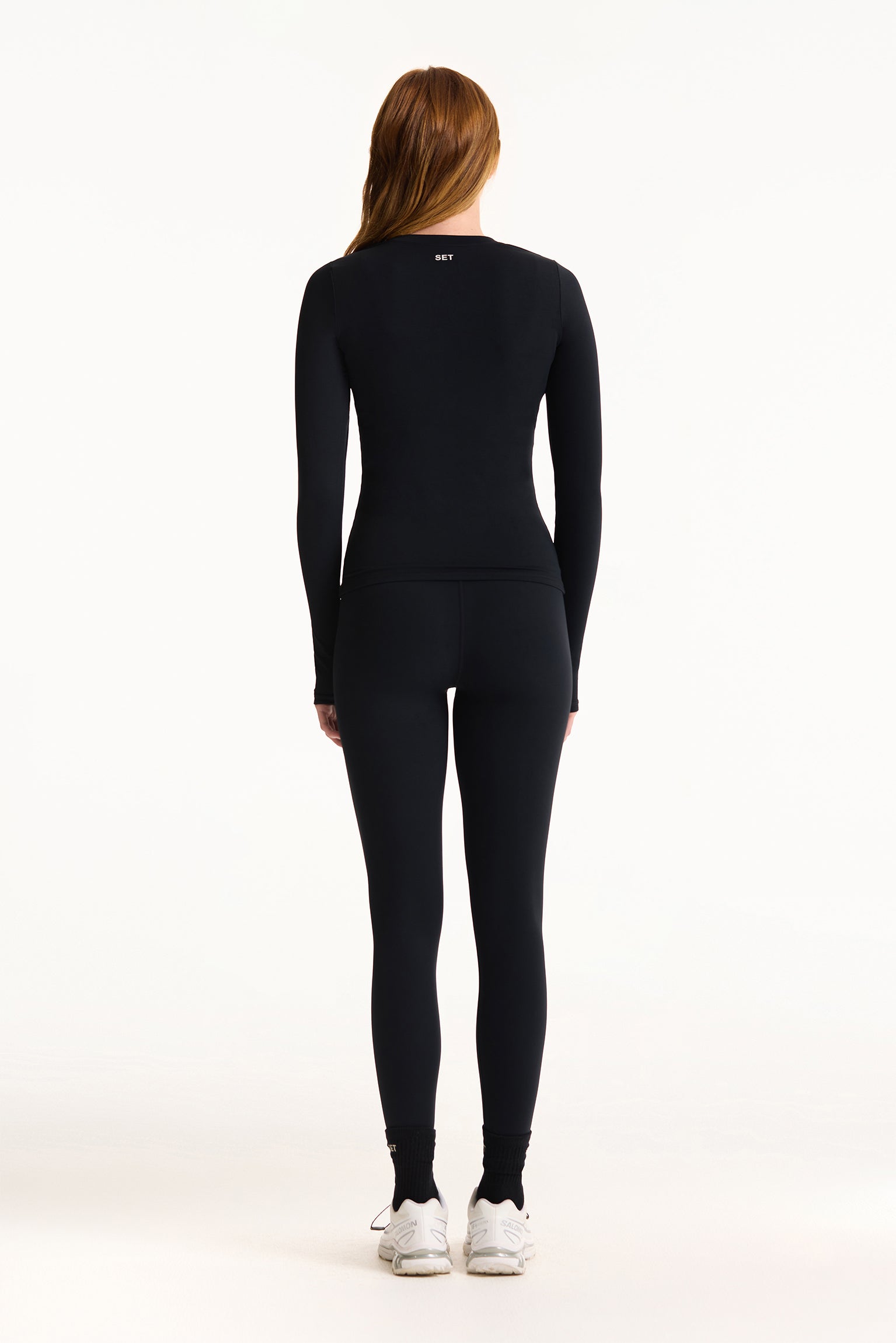 Person wearing a black long-sleeve top and leggings set on a white background