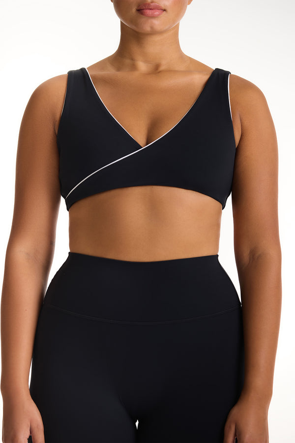 Black sports bra with white trim worn by a model on a white background