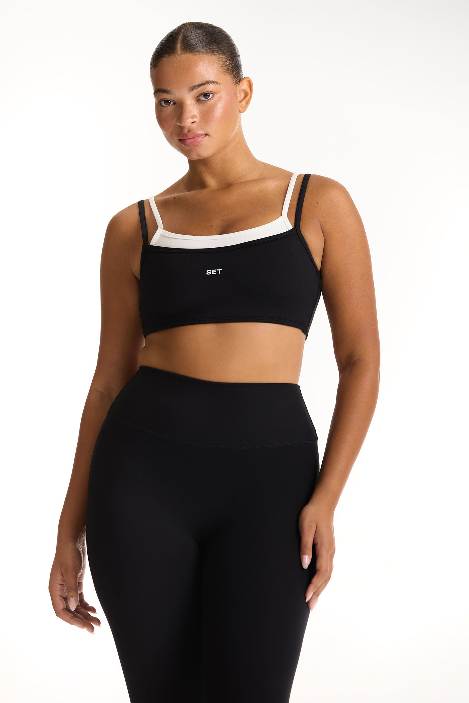 Woman wearing a black sports bra and leggings set on a white background 
