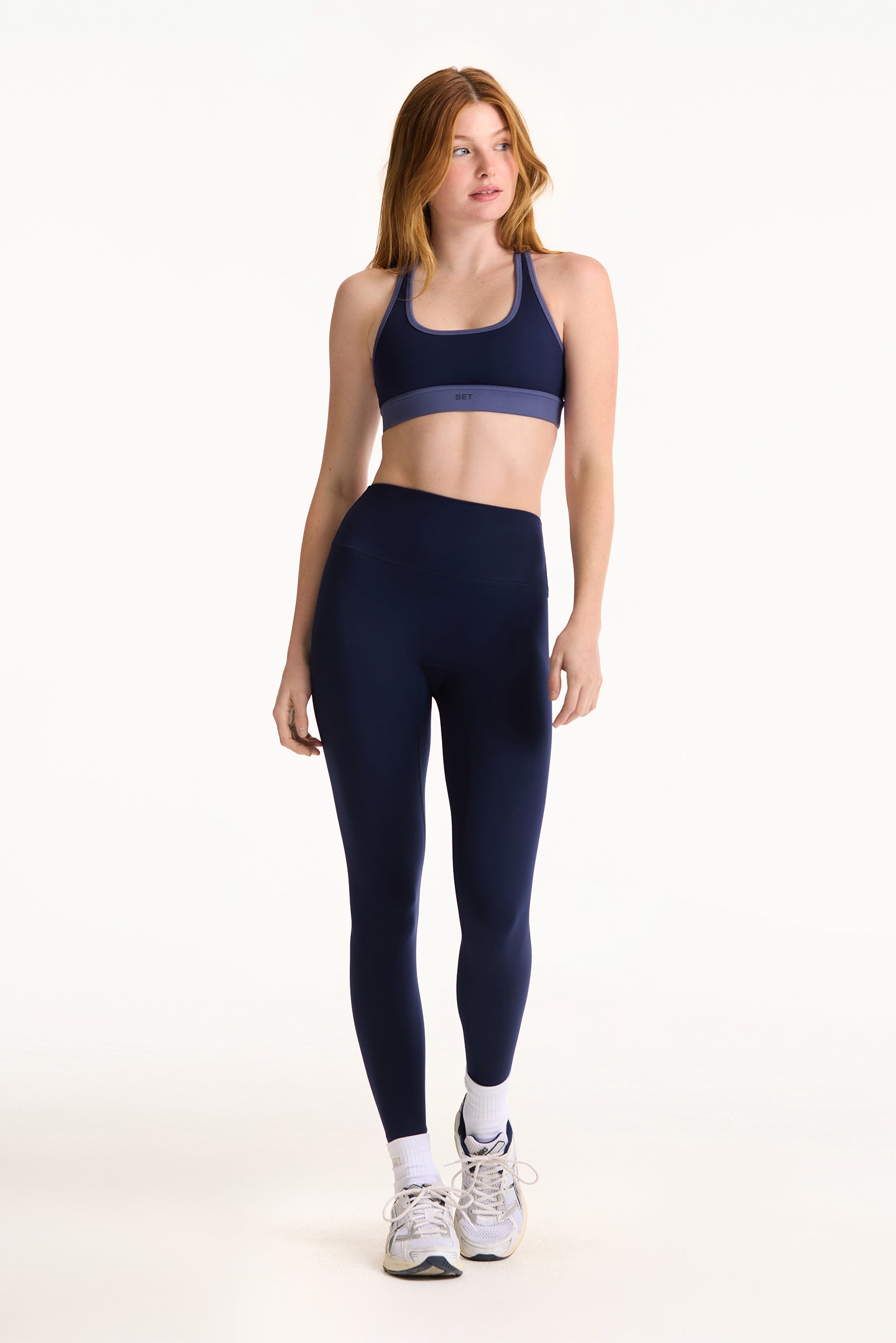 Woman wearing a navy sports bra and leggings set on a white background