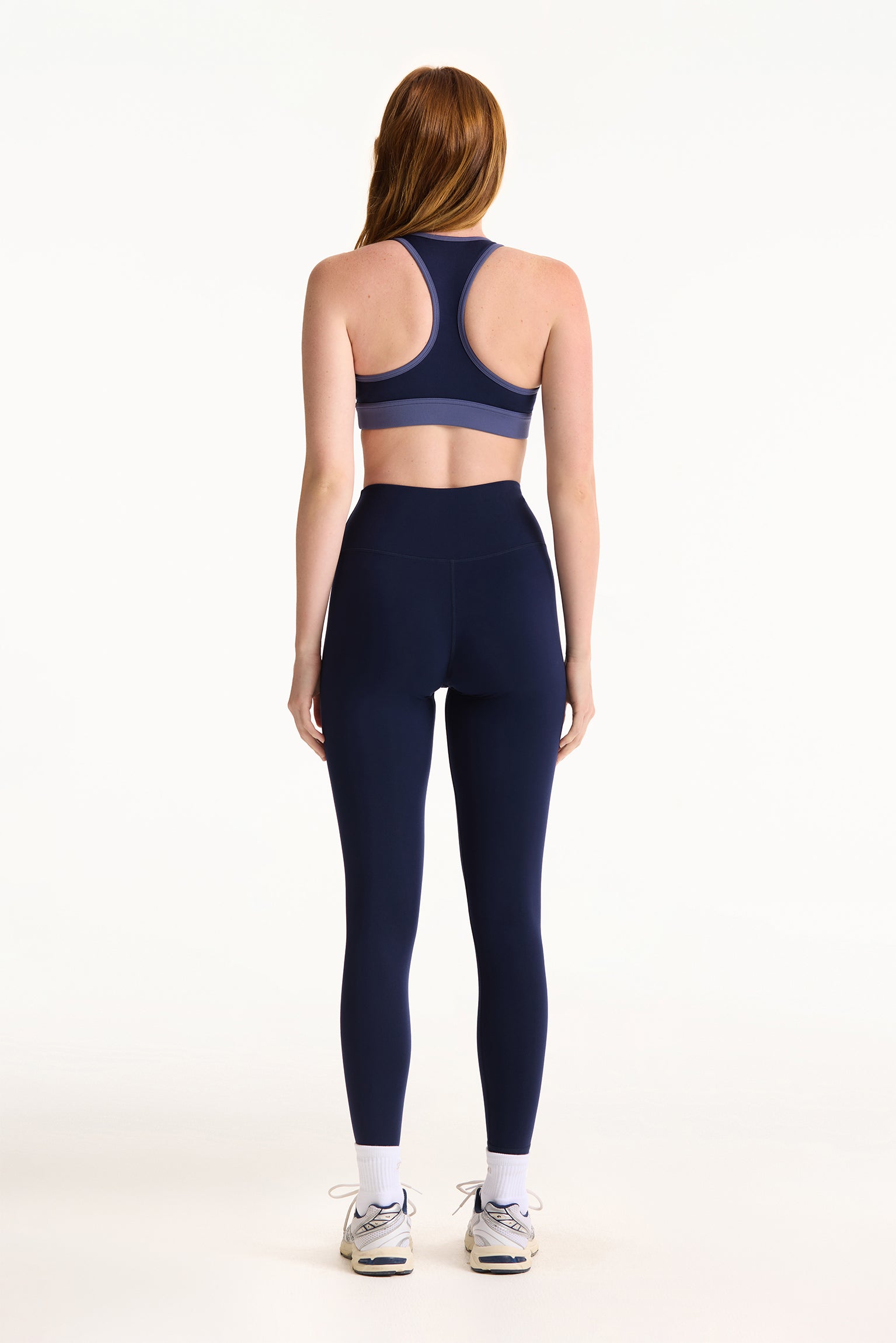 Woman wearing a navy sports bra and leggings set on a white background