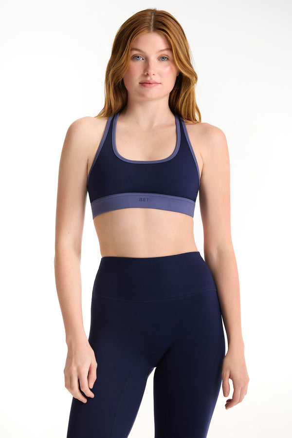 Woman wearing a navy sports bra and leggings on a white background 
