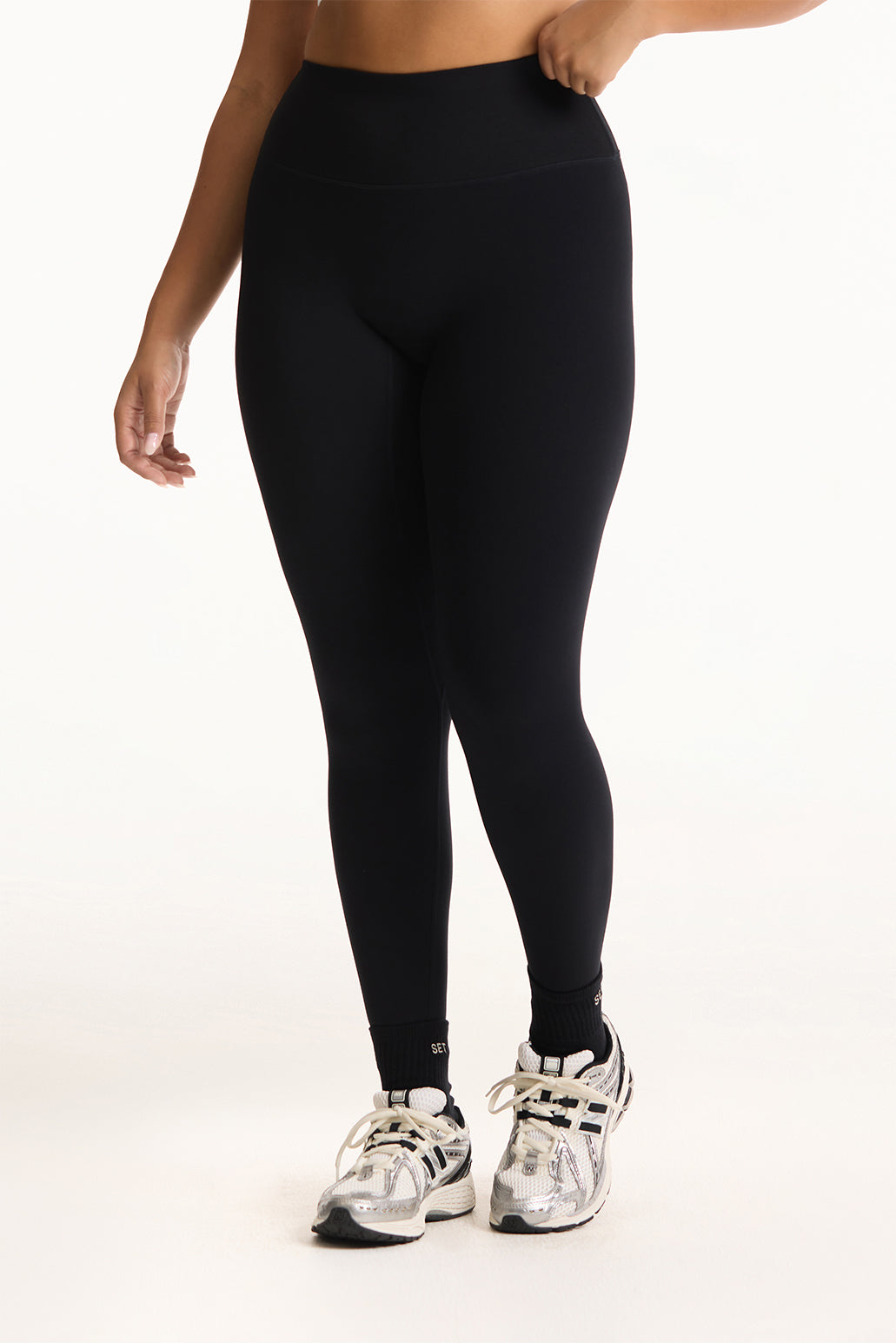 Person wearing black leggings and silver athletic shoes on a white background <model-info>Jade wears a size L and is 5’9”, 30” waist, 38” bust.</model-info>