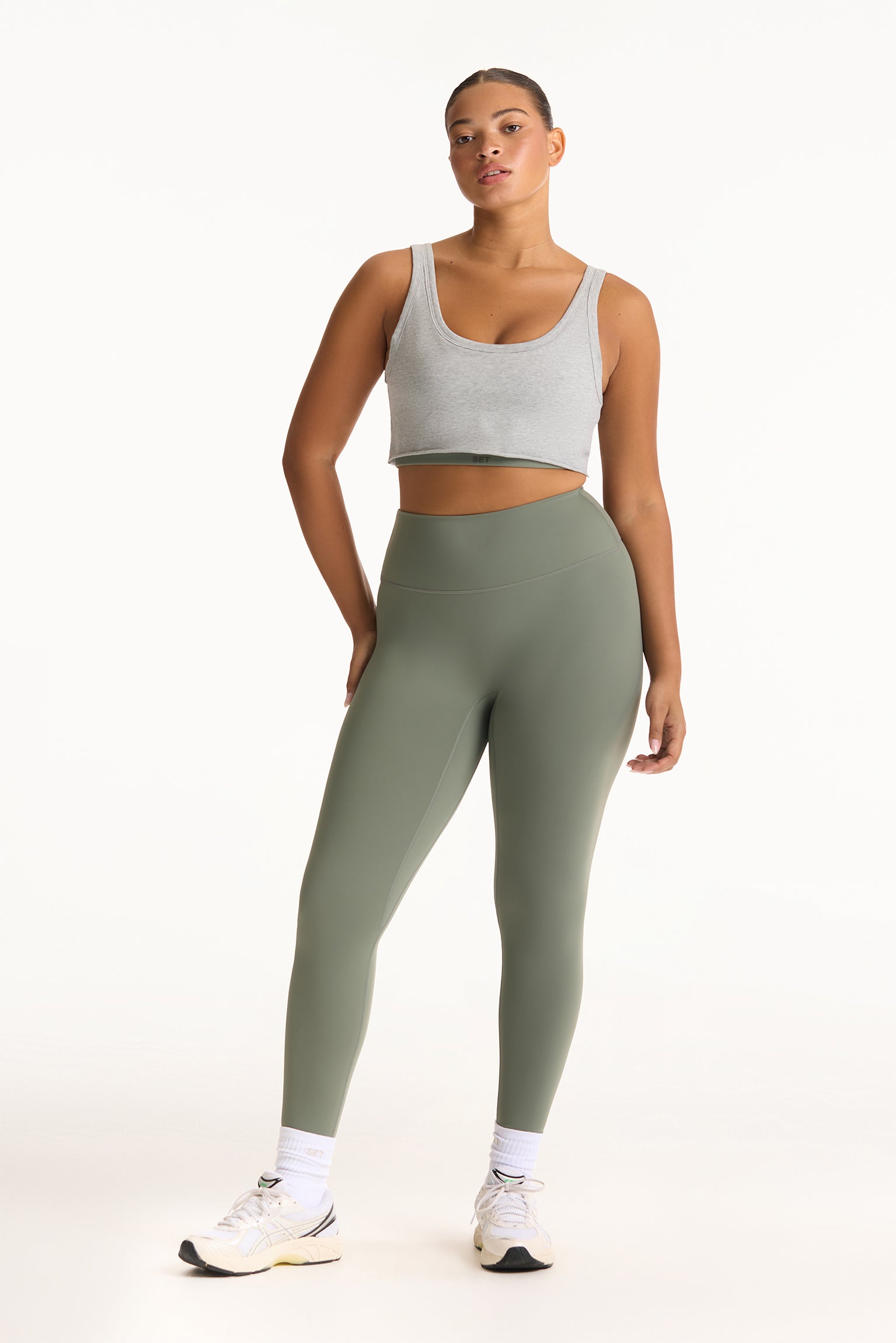 Woman wearing a gray tank top and green leggings on a white background