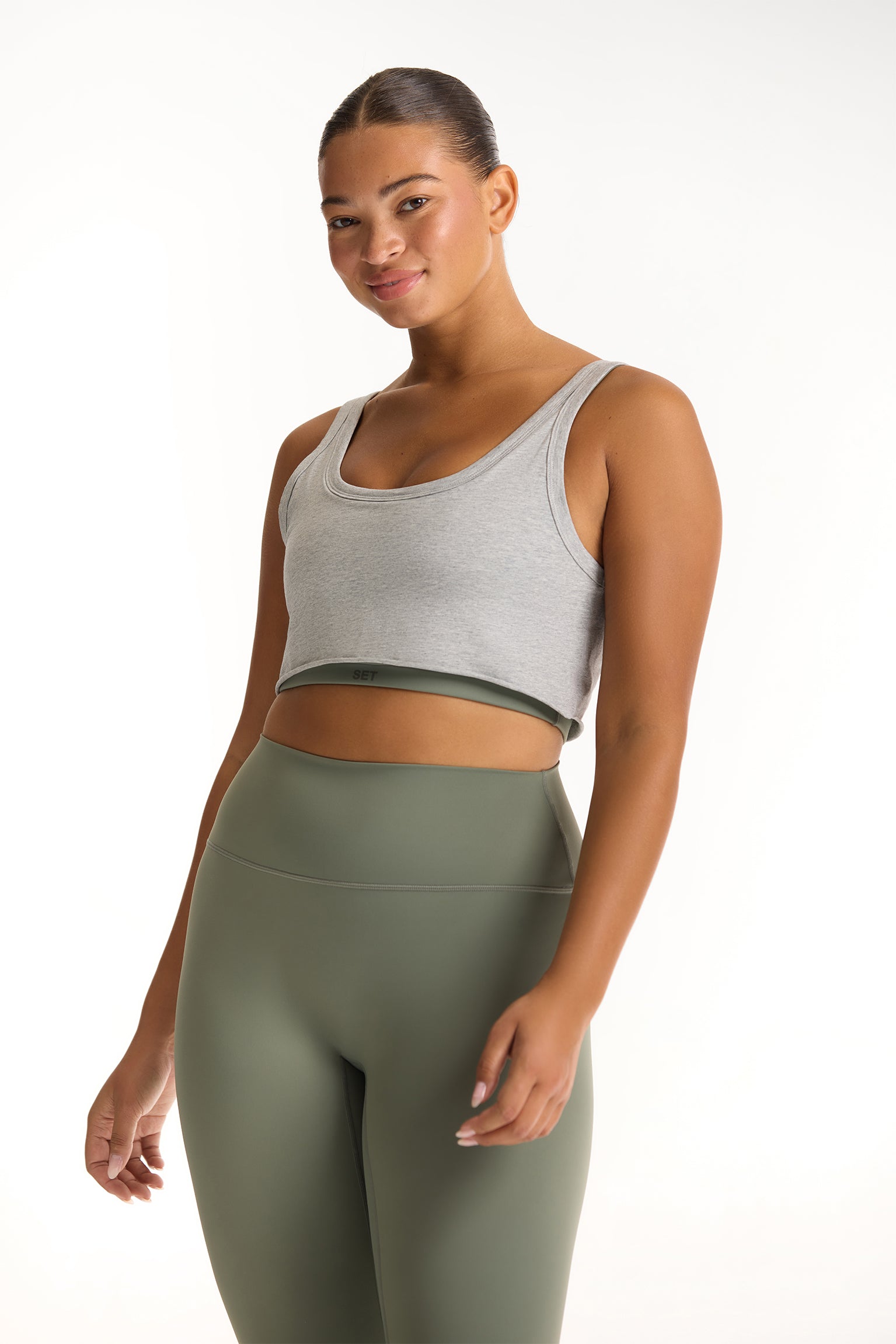 Woman wearing a gray sports bra and green leggings on a white background <model-info>Jade wears a size L and is 5’9”, 30” waist, 38” bust.</model-info>