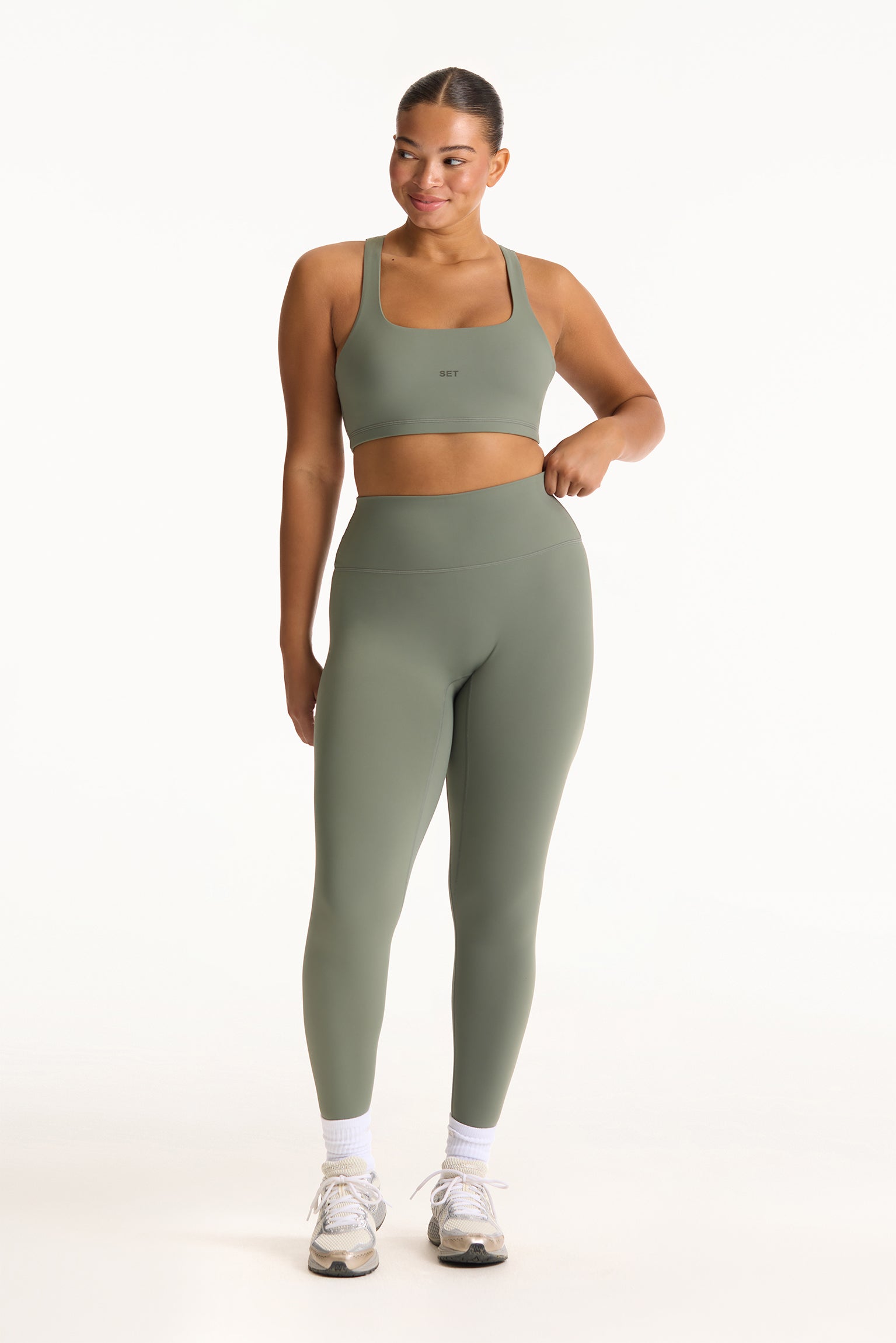 Woman wearing a green sports bra and leggings set on a white background