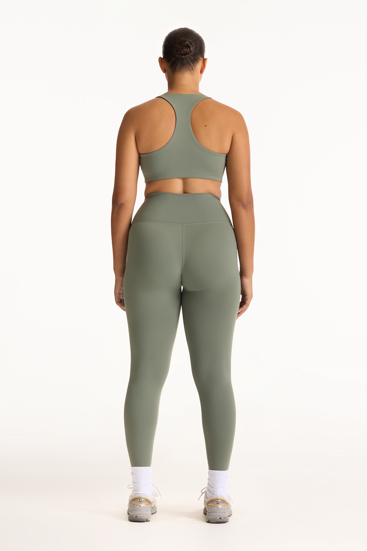 Person wearing a green sports bra and leggings set on a white background