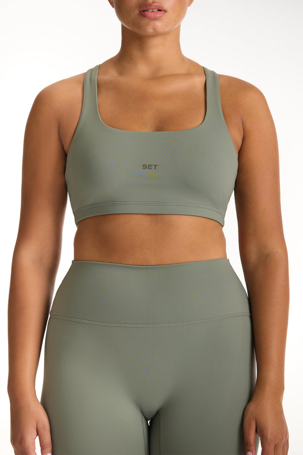 Person wearing a green sports bra and leggings set on a white background