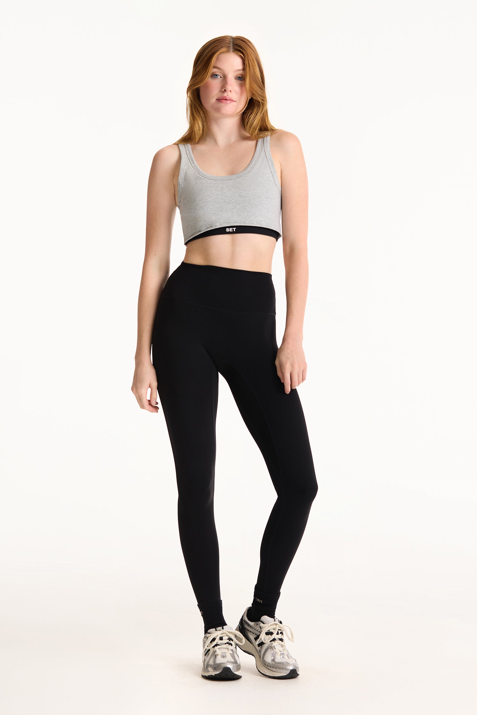 Woman wearing a gray sports bra and black leggings on a white background