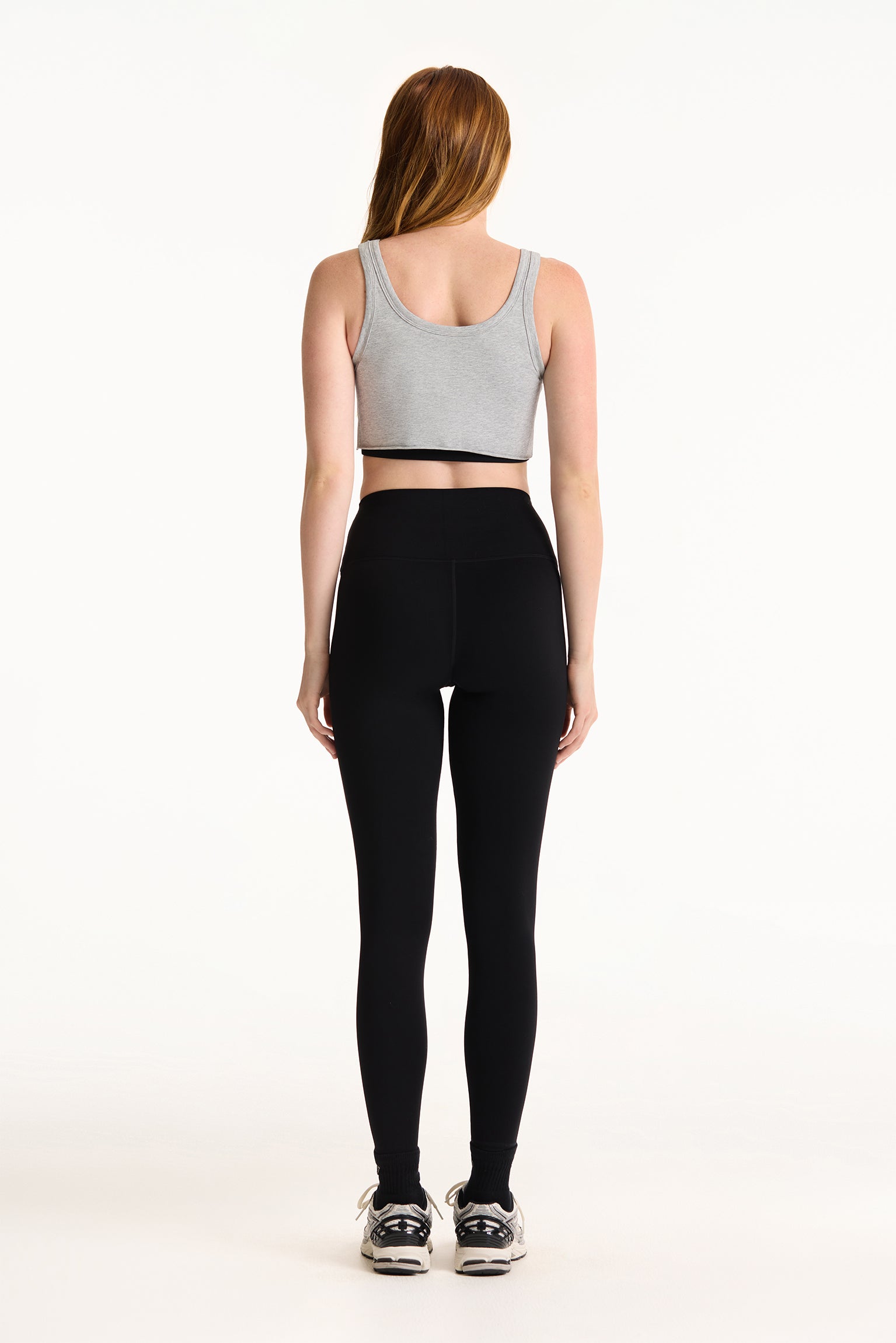 Person wearing a gray sports bra and black leggings on a white background