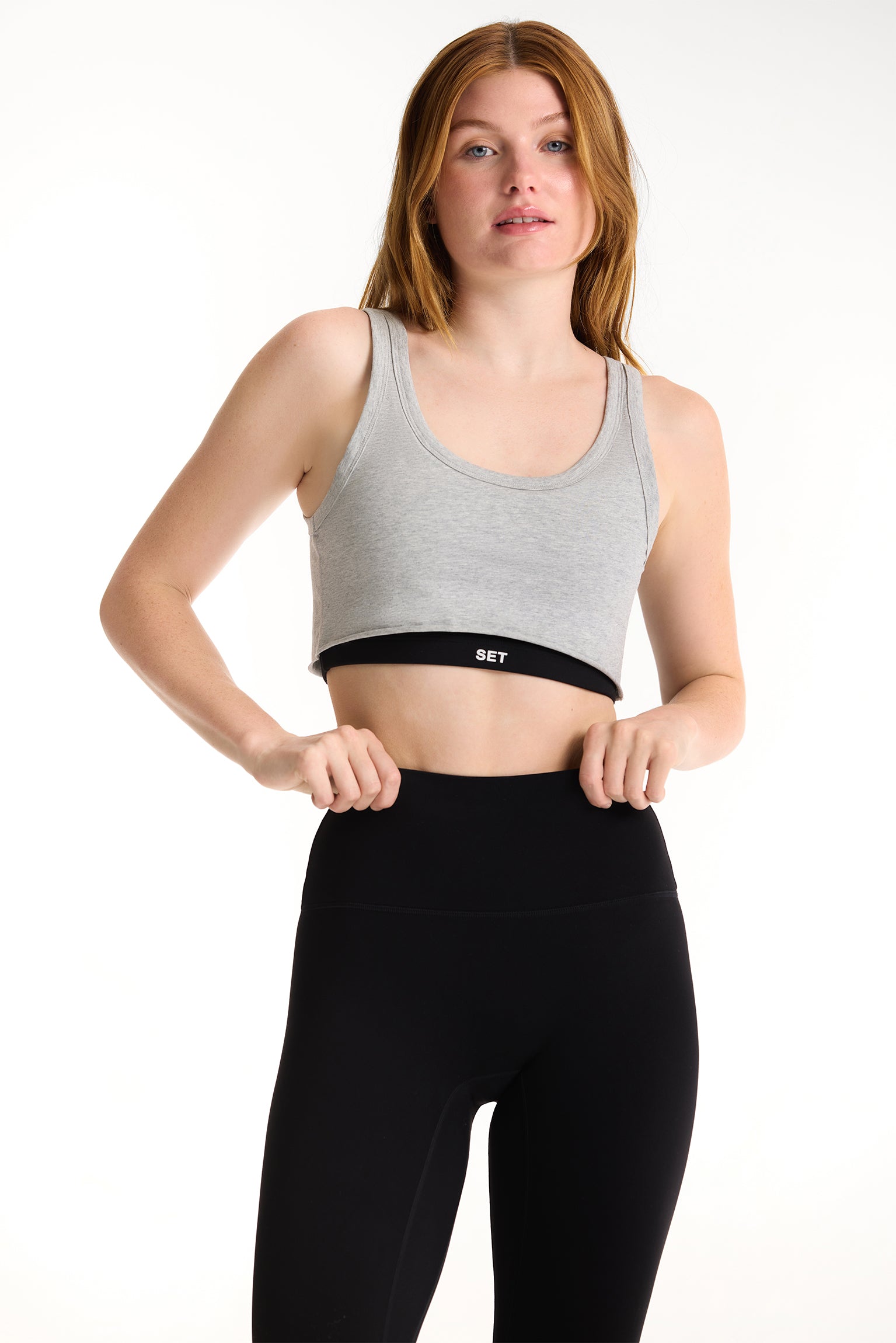 Woman wearing a gray sports bra and black leggings on a white background 