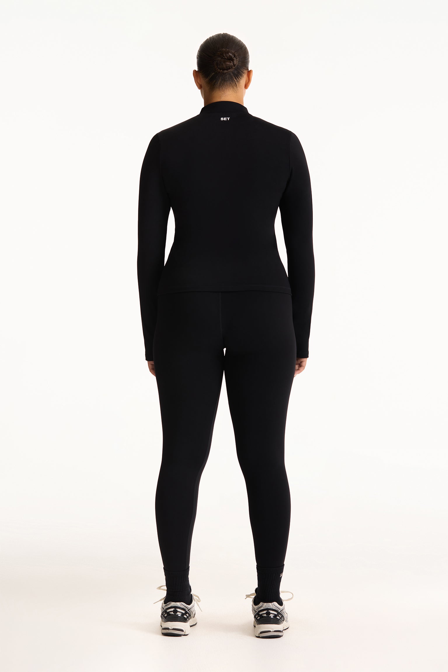 Person wearing a black long-sleeve top and leggings on a white background