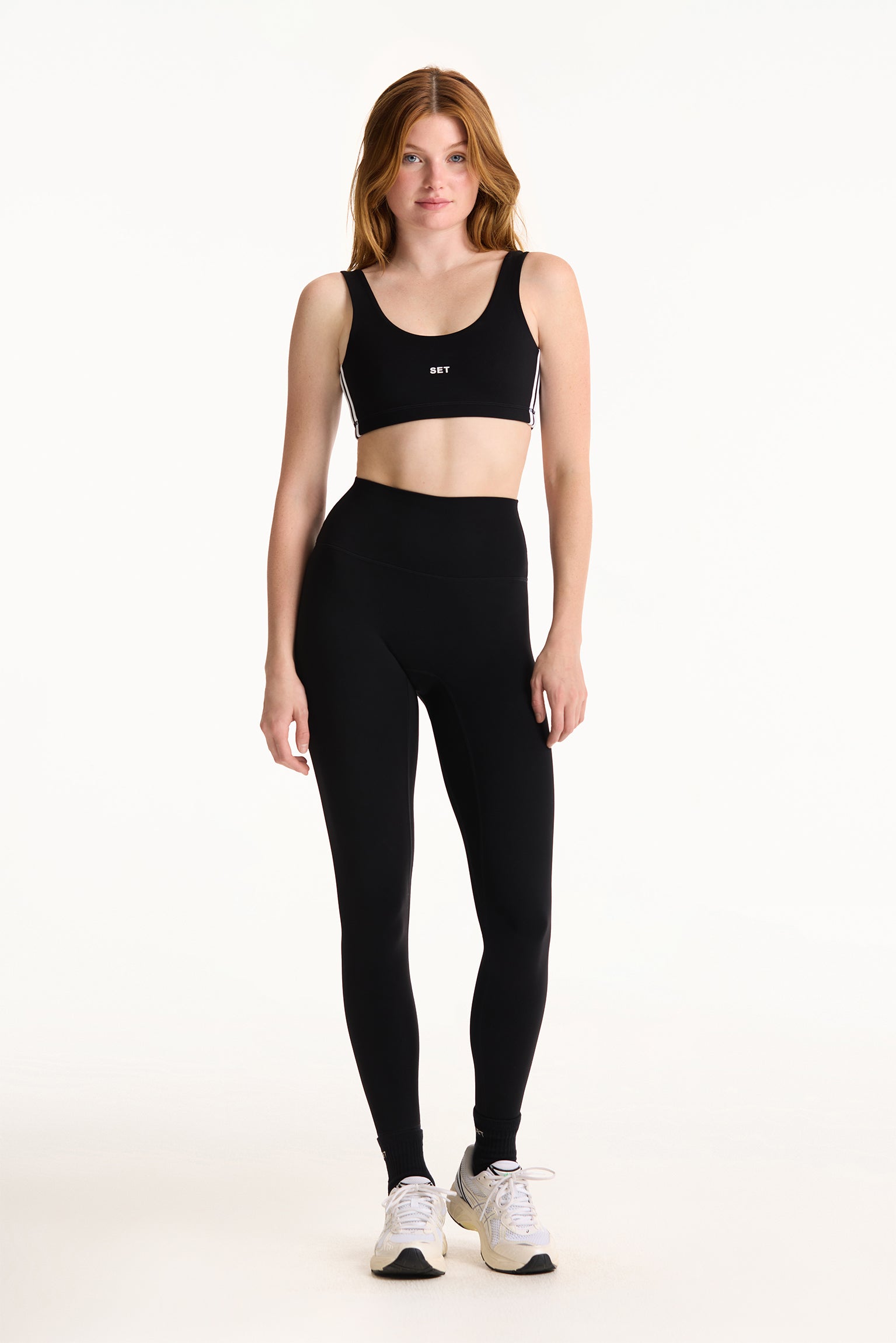 Woman wearing a black sports bra and leggings on a white background