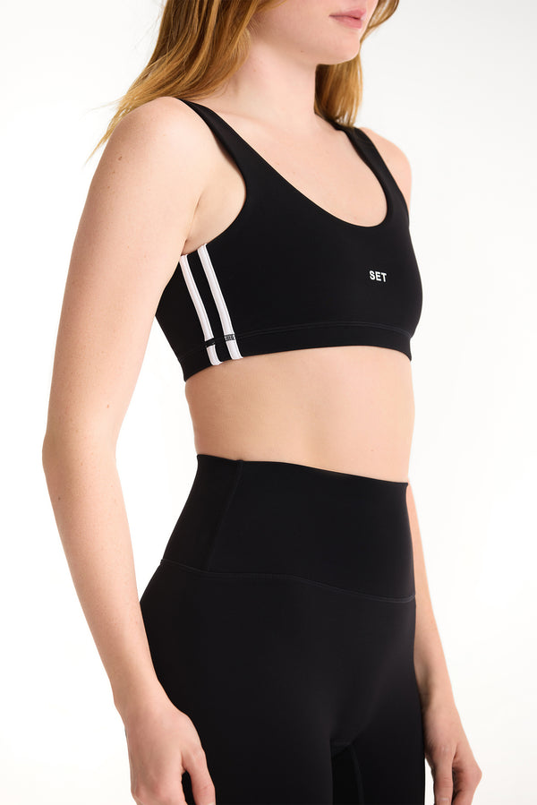 Black sports bra with white stripes on a model against a white background