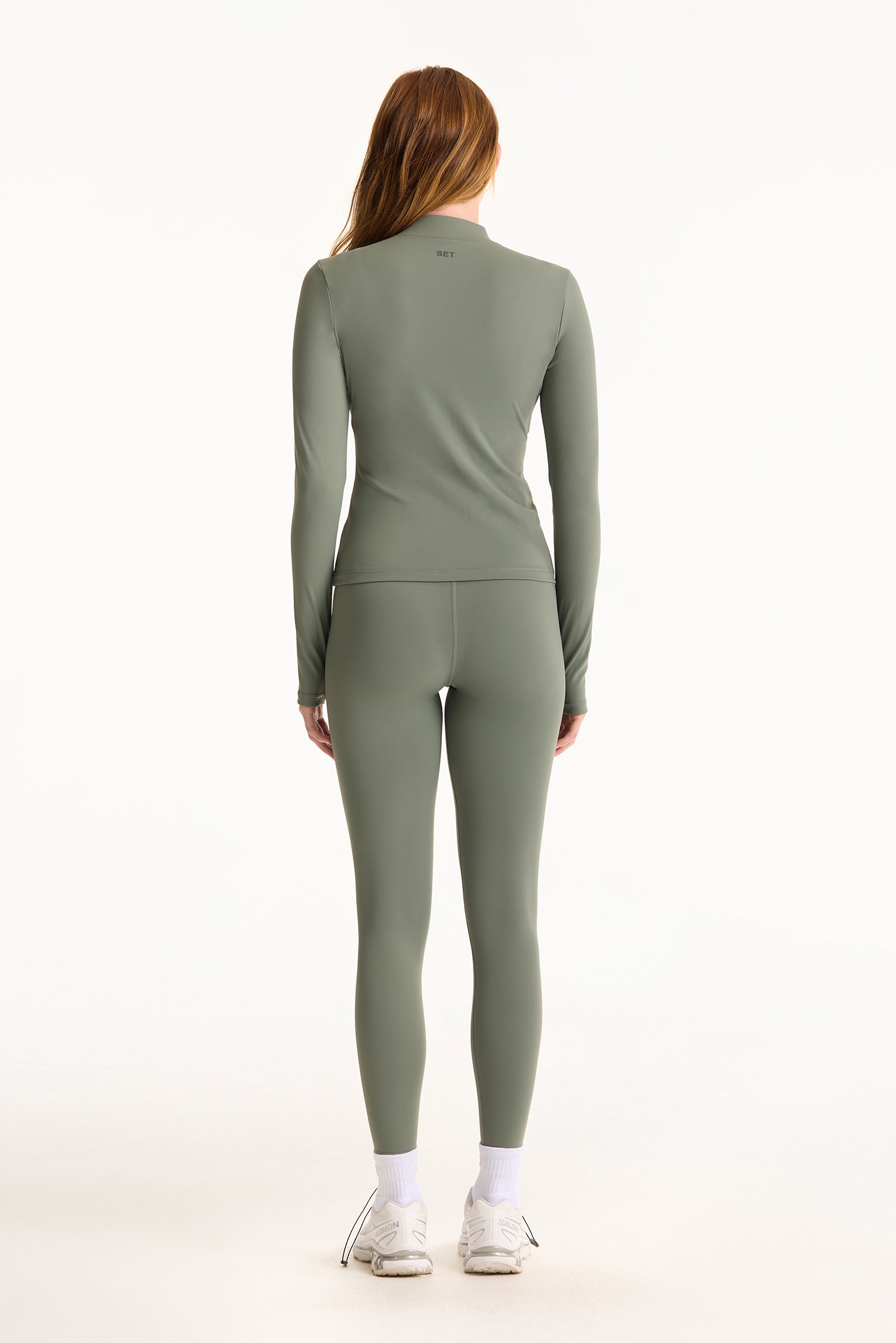 Person wearing a green long-sleeve top and leggings set on a white background
