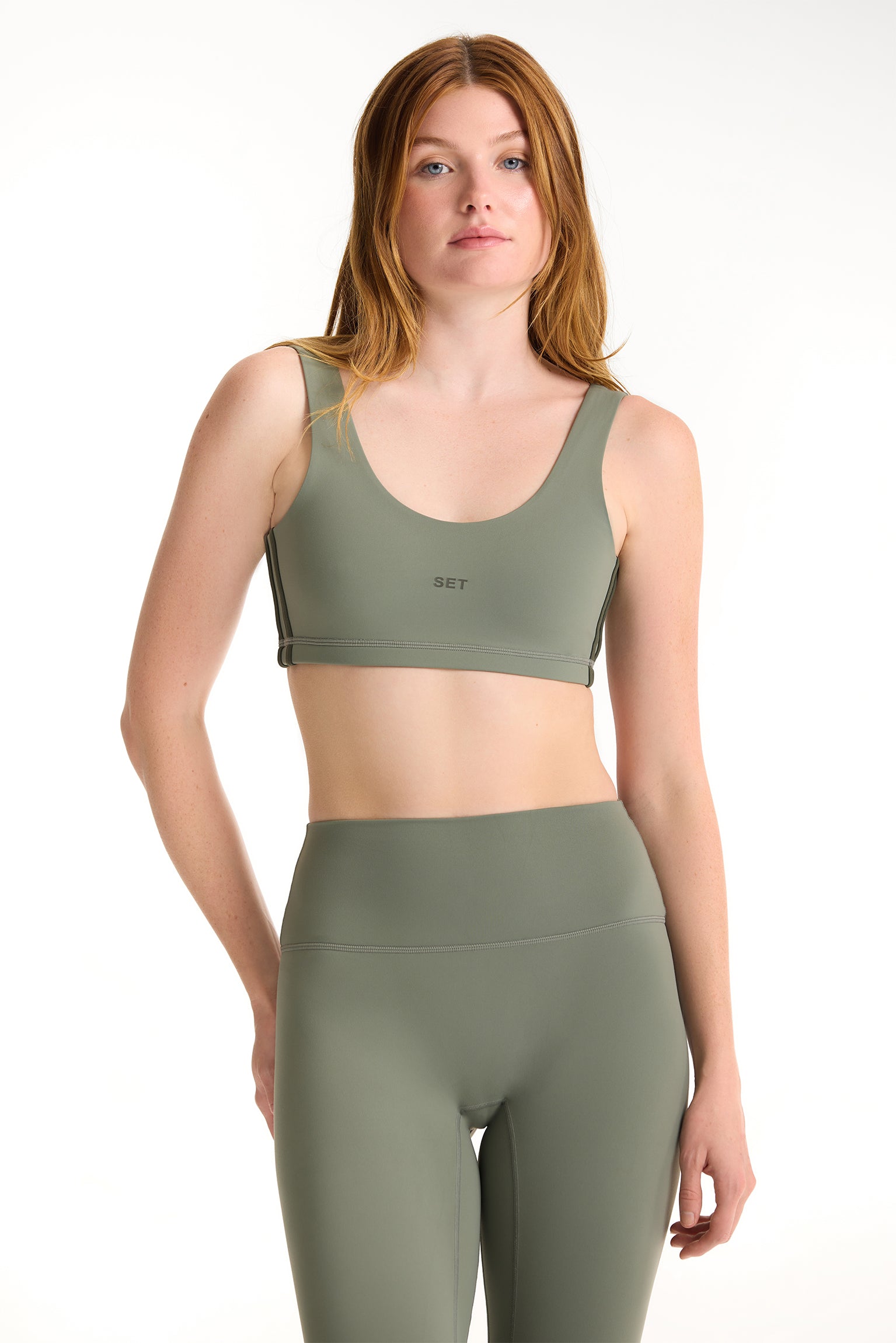 Woman wearing a green sports bra and leggings set on a white background 