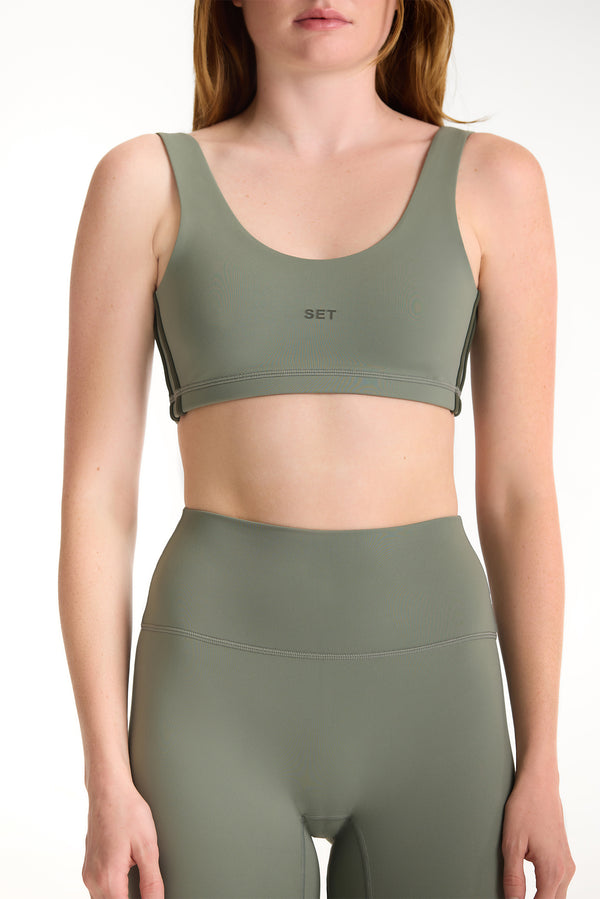 Person wearing a green sports bra and leggings set on a white background