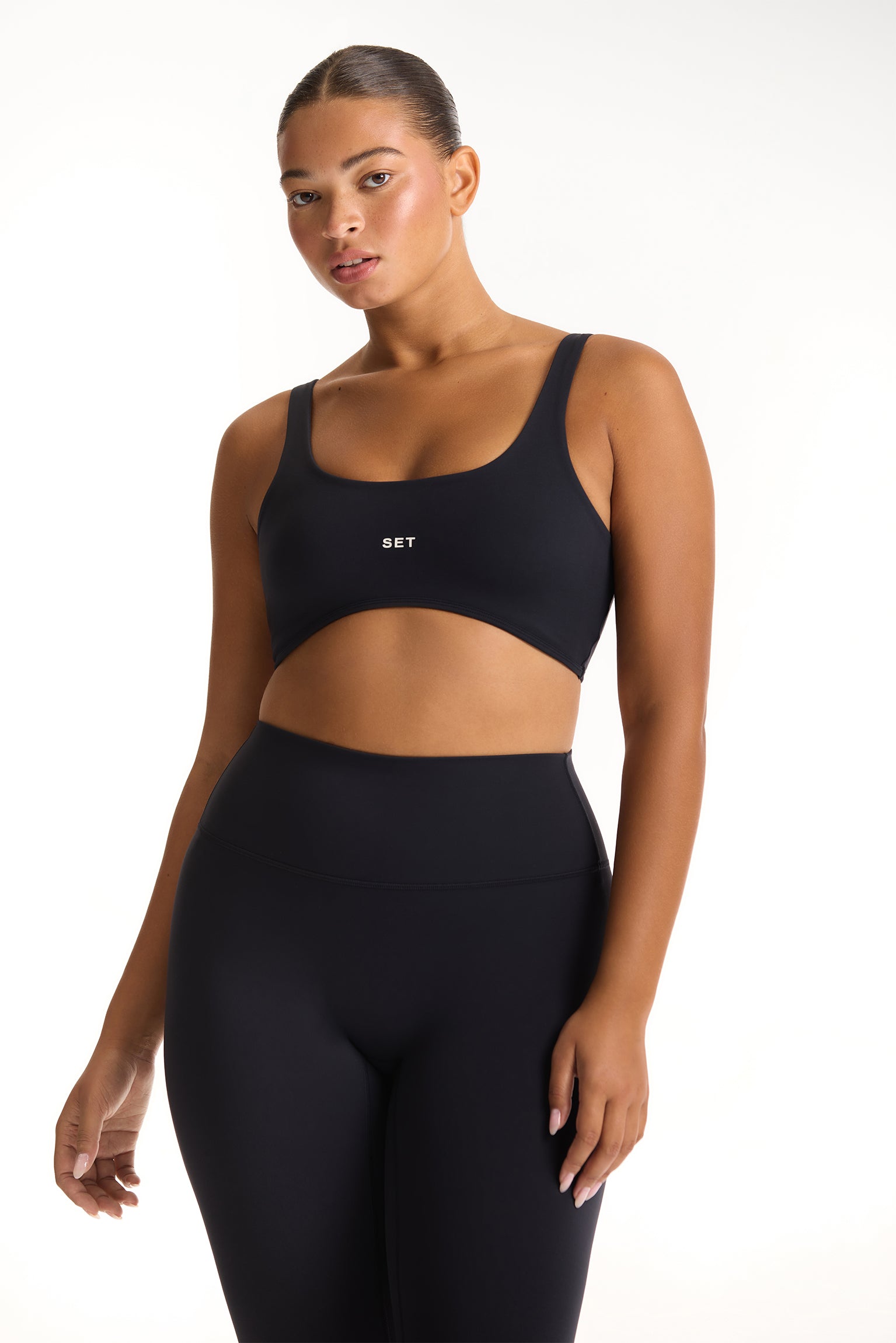 Woman wearing a black sports bra and leggings with 'SET' branding on a white background 