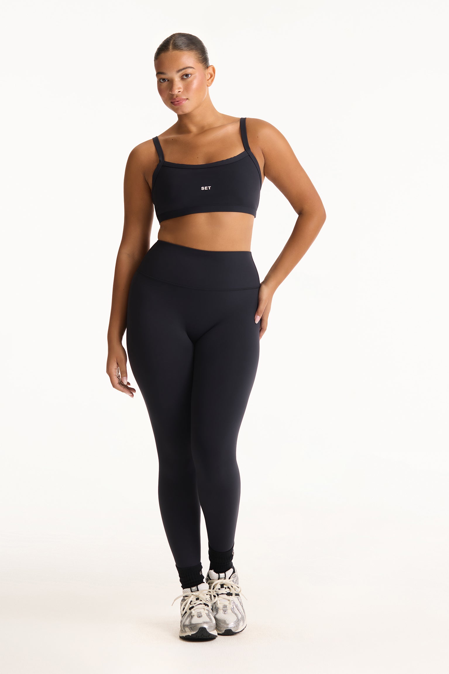 Woman wearing a black sports bra and leggings set on a white background