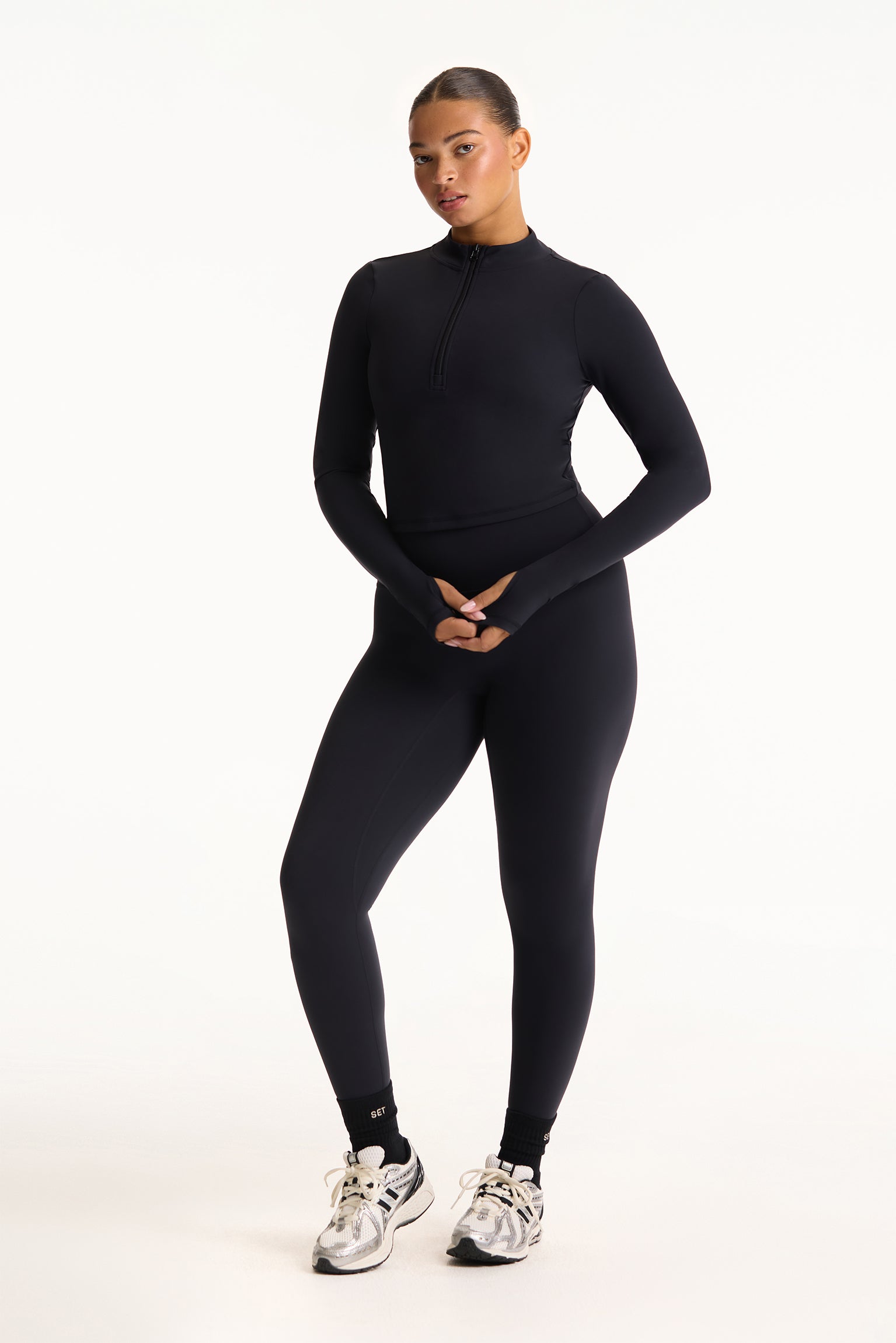 Person wearing a black long-sleeve top and leggings on a white background