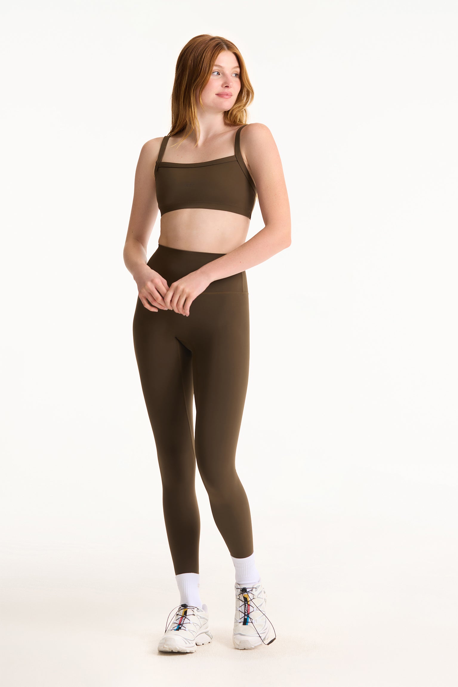 Woman wearing a brown sports bra and leggings set on a white background