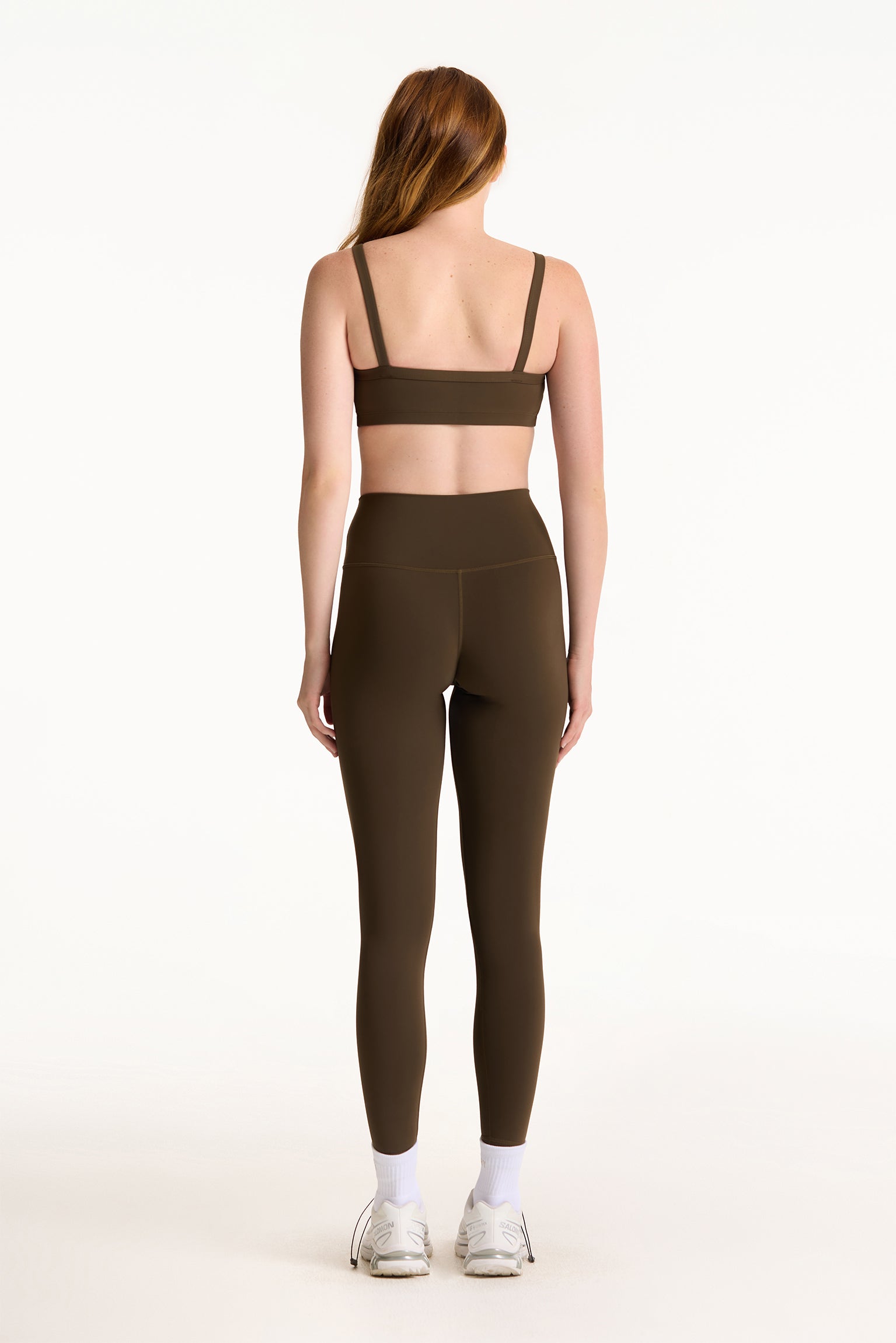 Woman wearing a brown sports bra and leggings set on a white background