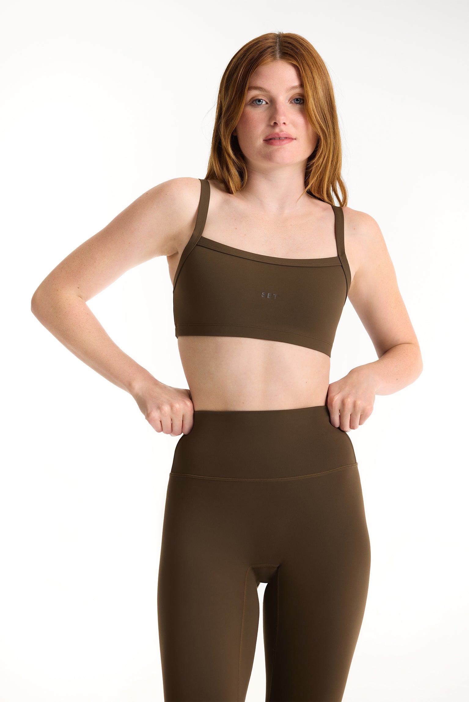 Woman wearing a brown sports bra and leggings set on a white background <model-info>Dickey wears a size S and is 5’9”, 24” waist, 32” bust.</model-info>