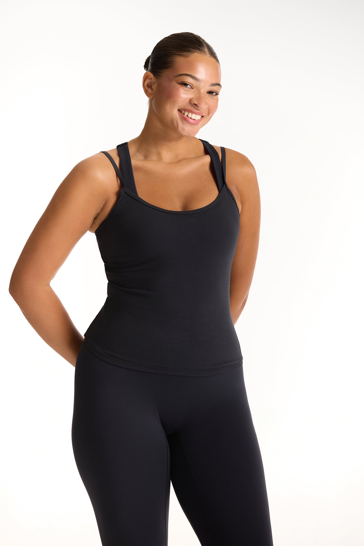 Woman wearing a black tank top and leggings on a white background 
