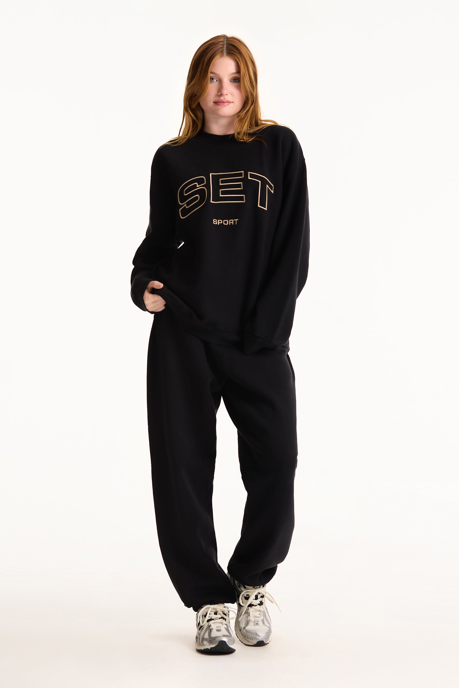 Person wearing a black 'SET' sweatshirt and pants on a white background