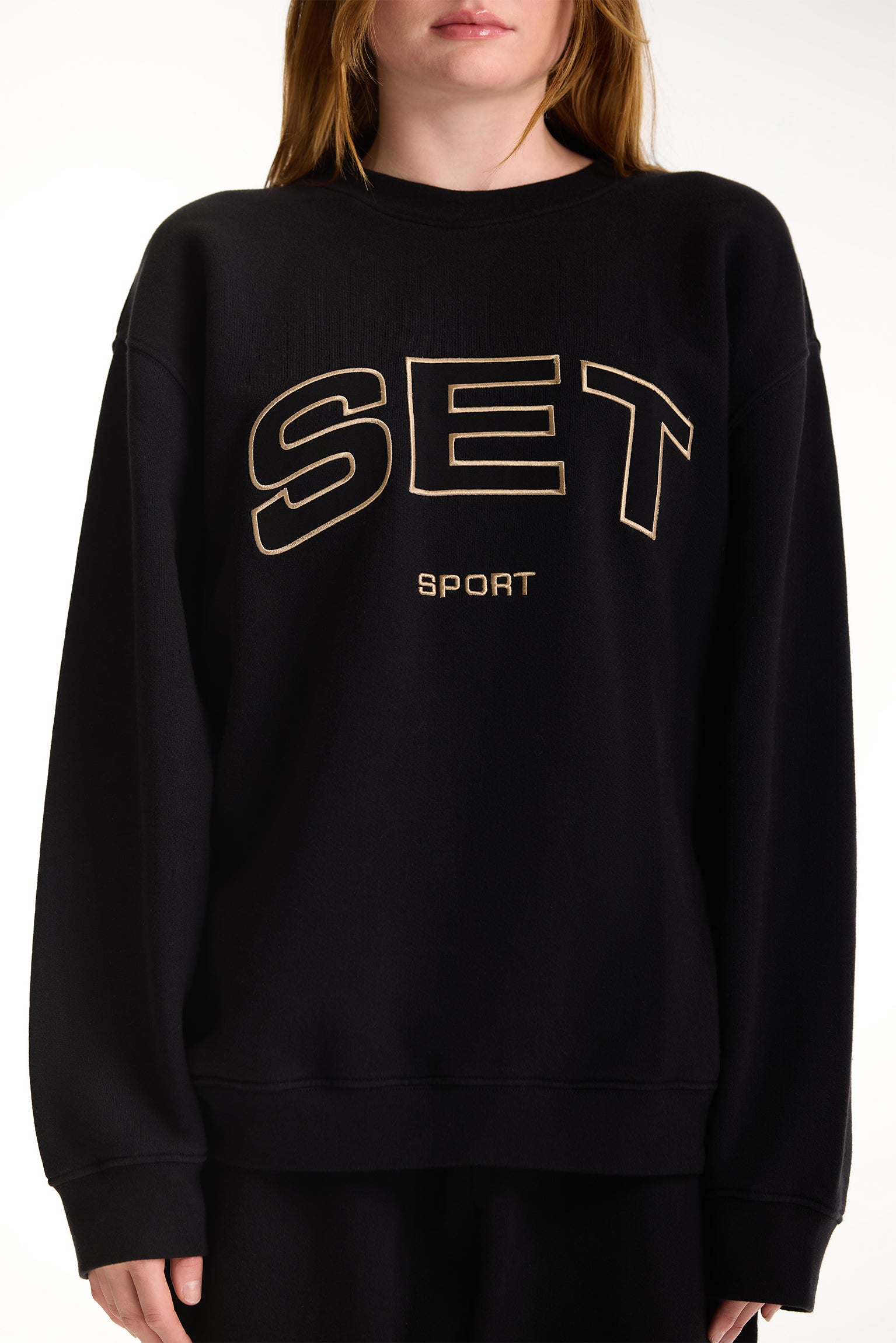 Black sweatshirt with 'SET Sport' text worn by a person on a white background