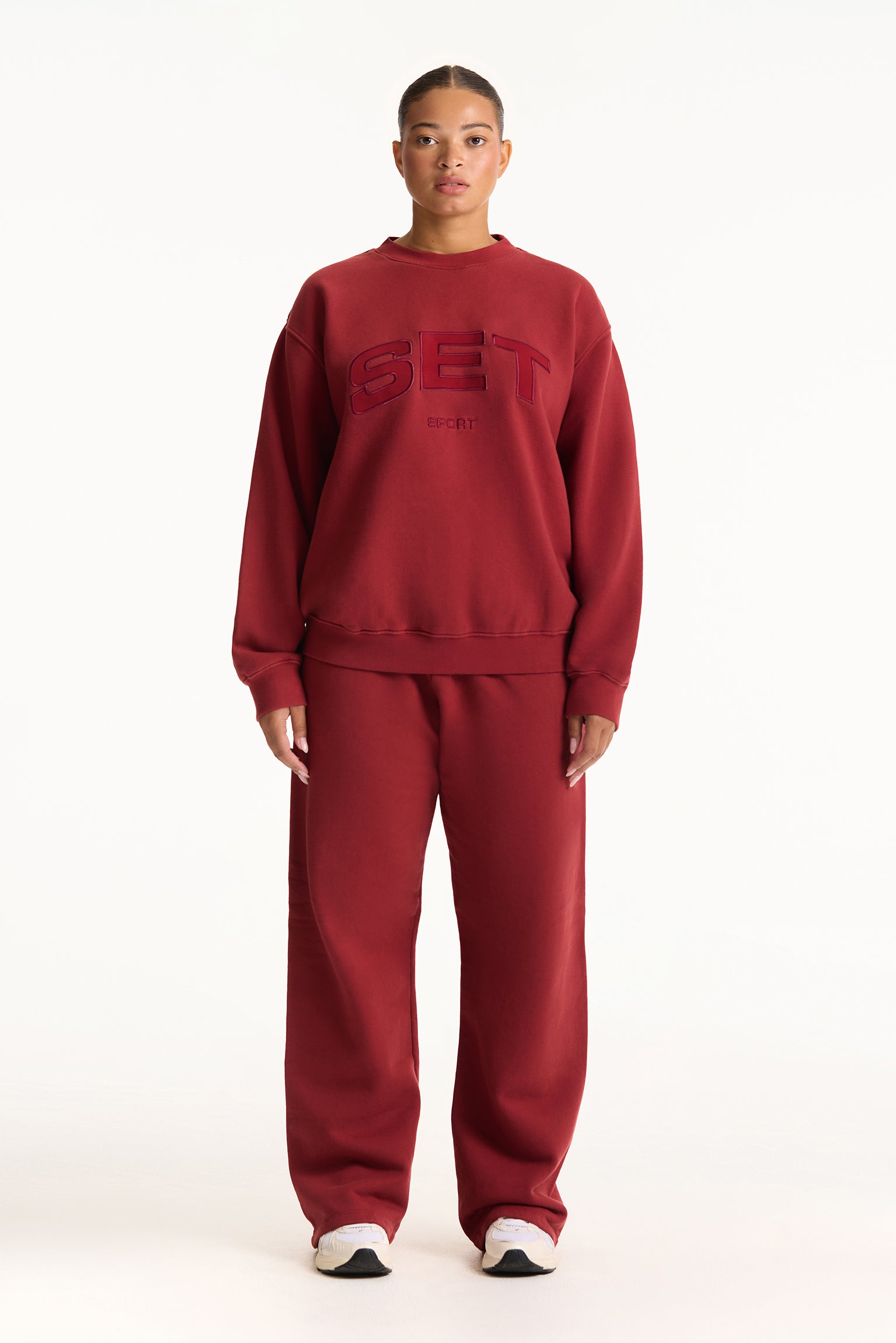 Person wearing a red sweatshirt and pants with 'SET' logo on a white background