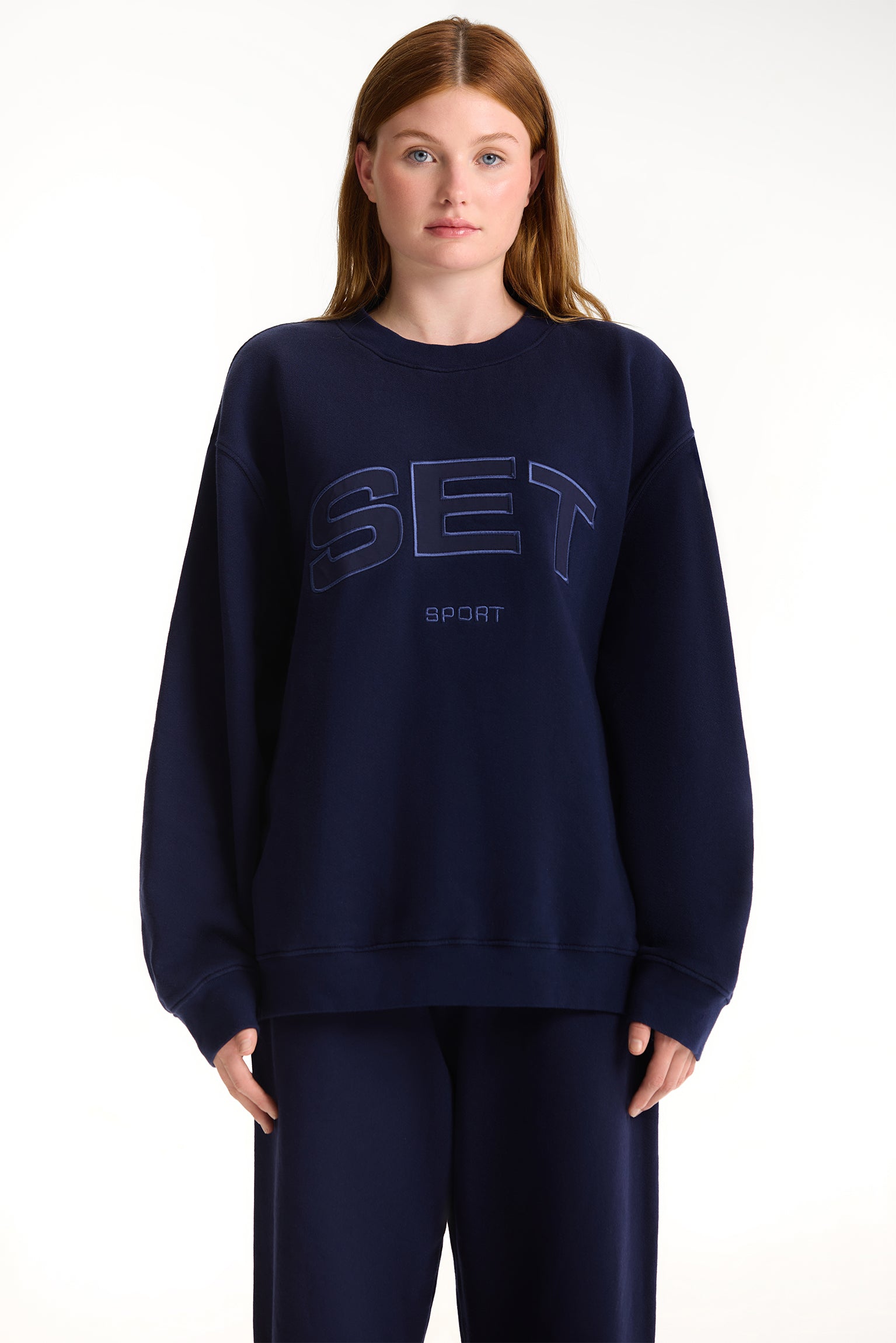 Person wearing a navy blue sweatshirt with 'SET' branding on a white background <model-info>Dickey wears a size L and is 5’9”, 24” waist, 32” bust.</model-info>