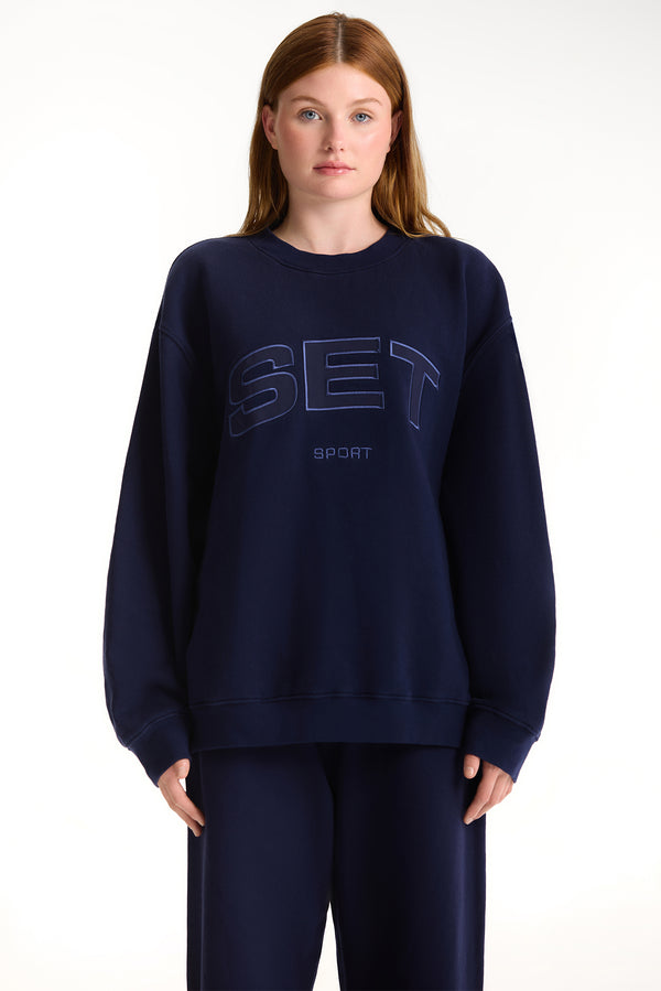 Person wearing a navy blue sweatshirt with 'SET' branding on a white background 
