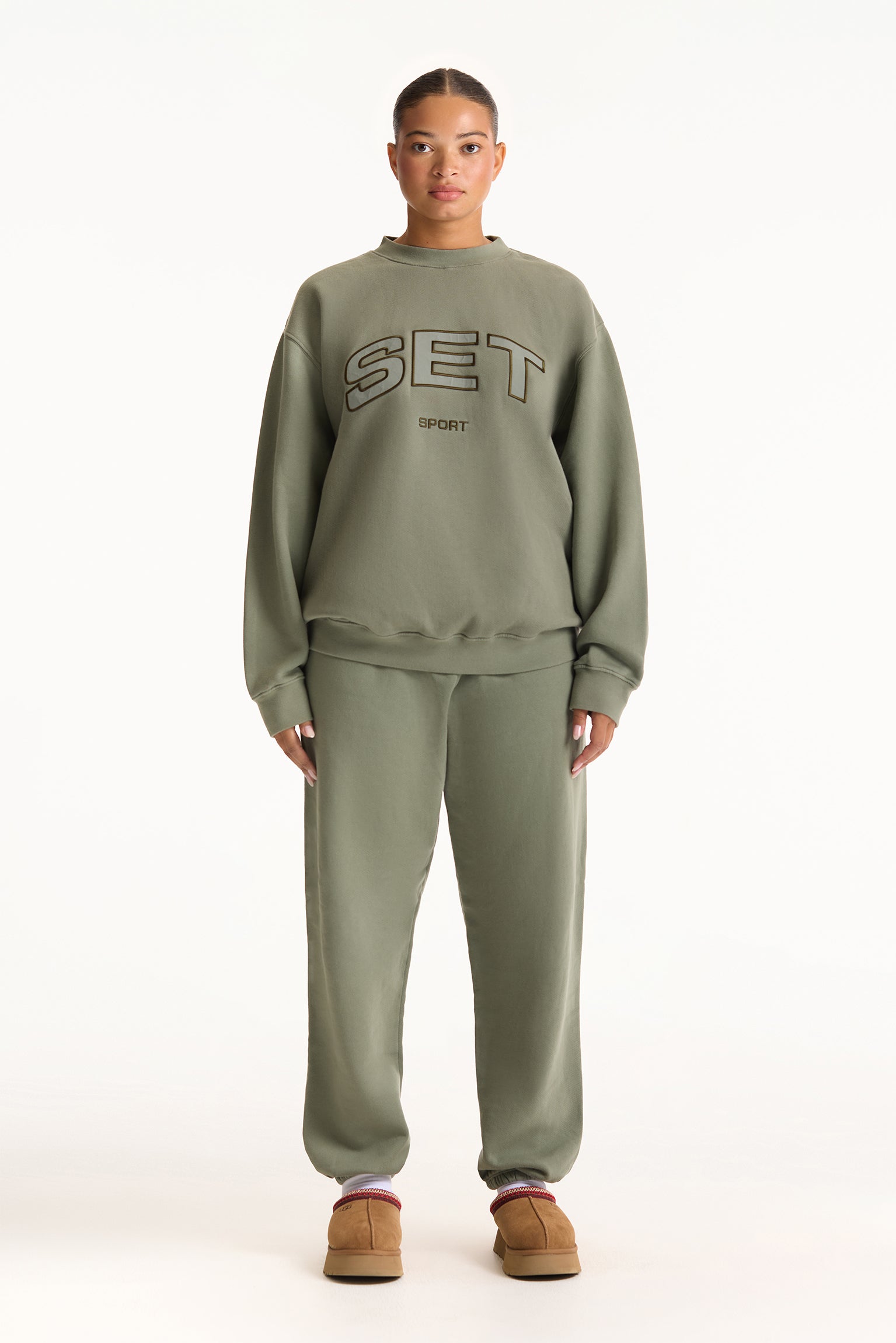 Person wearing a green 'SET' sweatshirt and pants on a white background