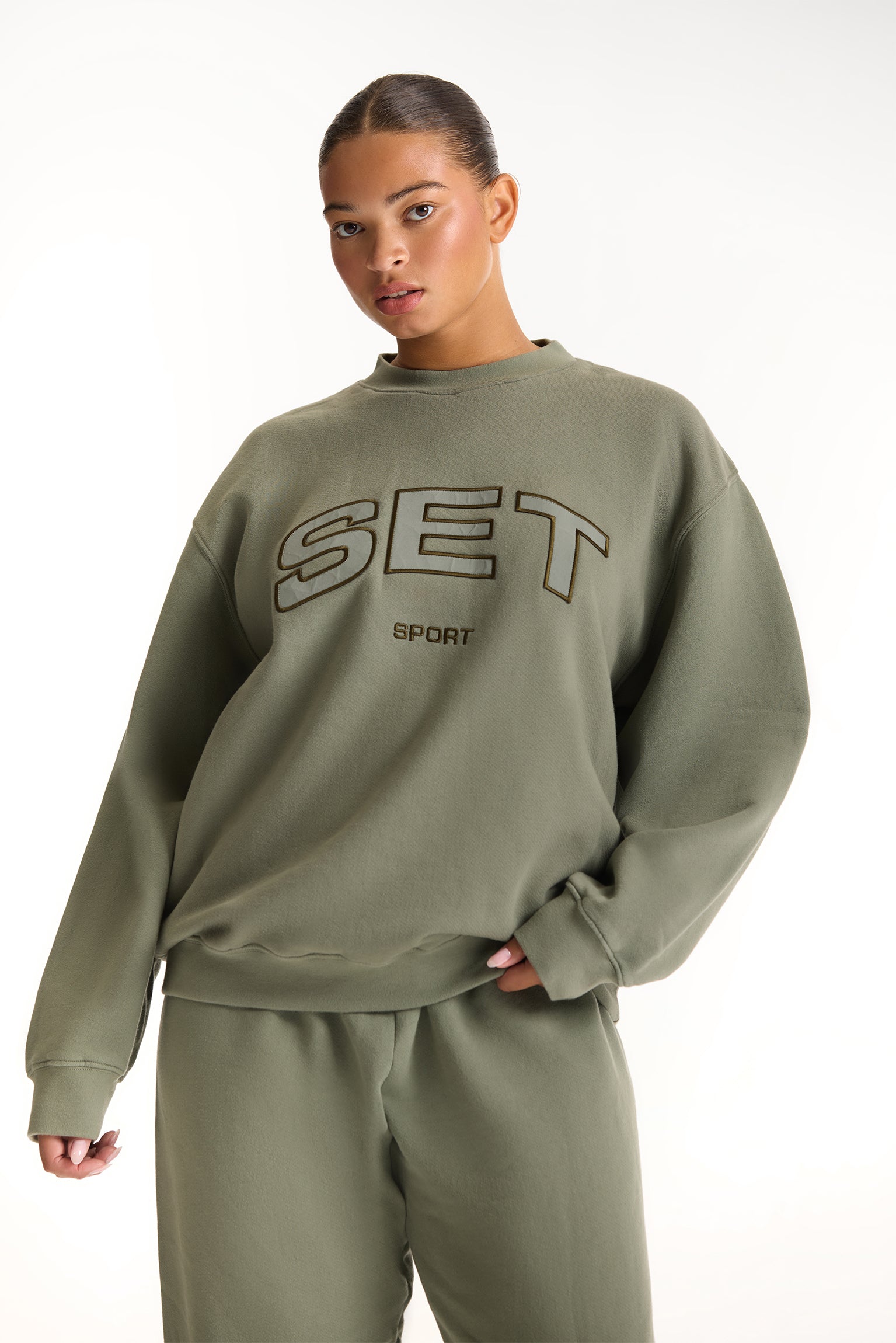 Person wearing a green 'SET Sport' sweatshirt on a white background <model-info>Jade wears a size L and is 5’9”, 30” waist, 38” bust.</model-info>