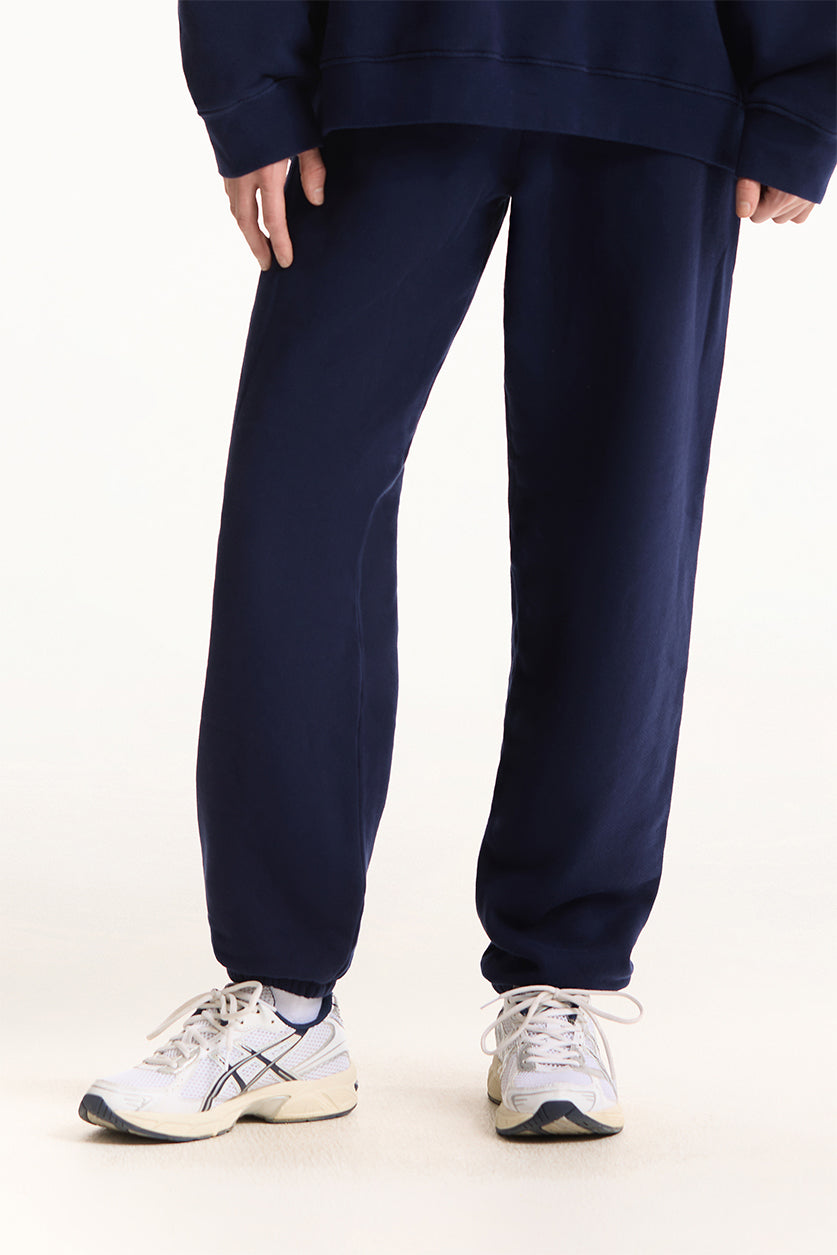 Person wearing navy blue sweatpants and white sneakers on a white background 