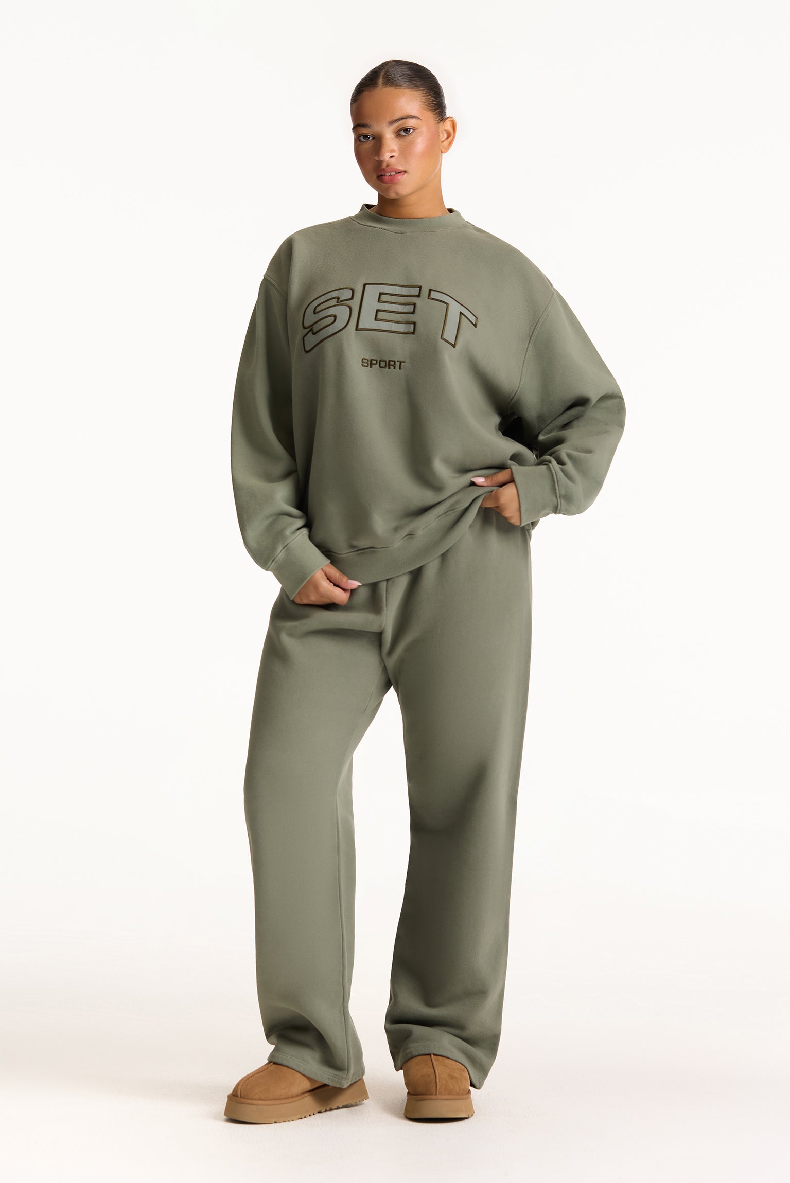 Person wearing a green 'SET' sweatshirt and pants on a white background