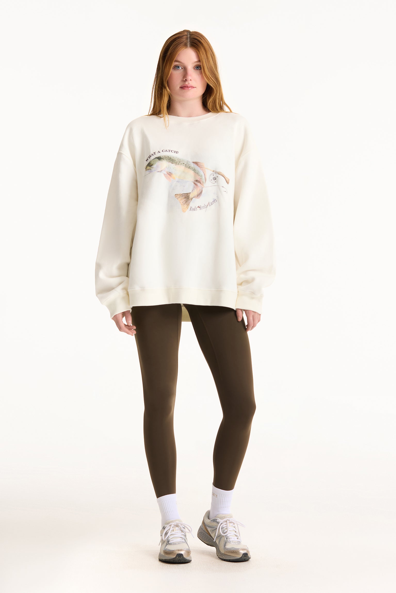 Person wearing a cream-colored sweatshirt with a graphic design and dark leggings on a white background