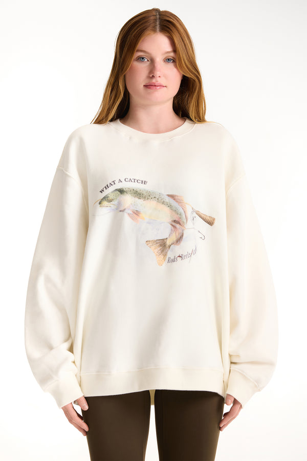 Woman wearing a cream-colored sweatshirt with a fish graphic and text on a white background 