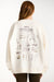 Person wearing a cream-colored sweatshirt with printed designs and text on the back.