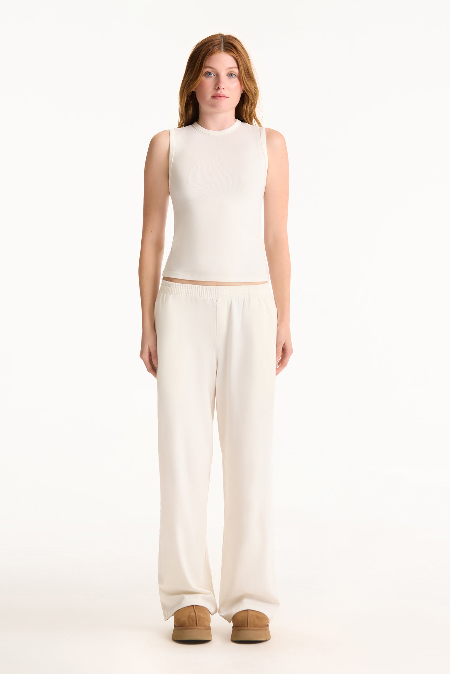 Woman wearing a white sleeveless top and wide-leg pants on a white background