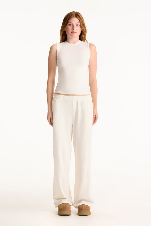 Woman wearing a white sleeveless top and wide-leg pants on a white background