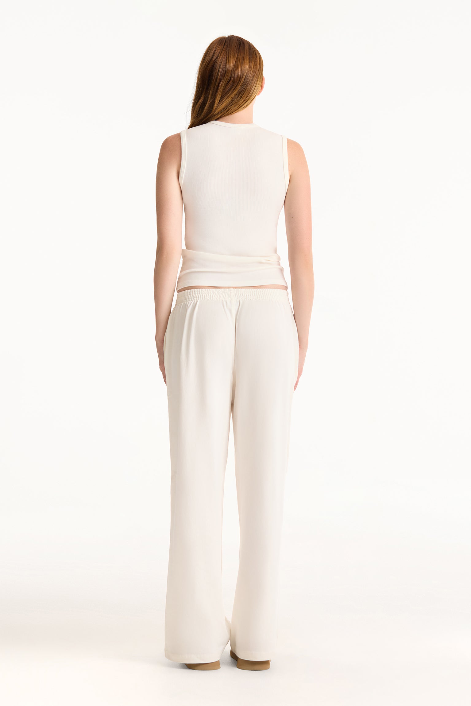 Woman wearing a white sleeveless top and wide-leg pants on a white background