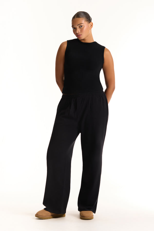 Person wearing a black sleeveless top and pants on a white background